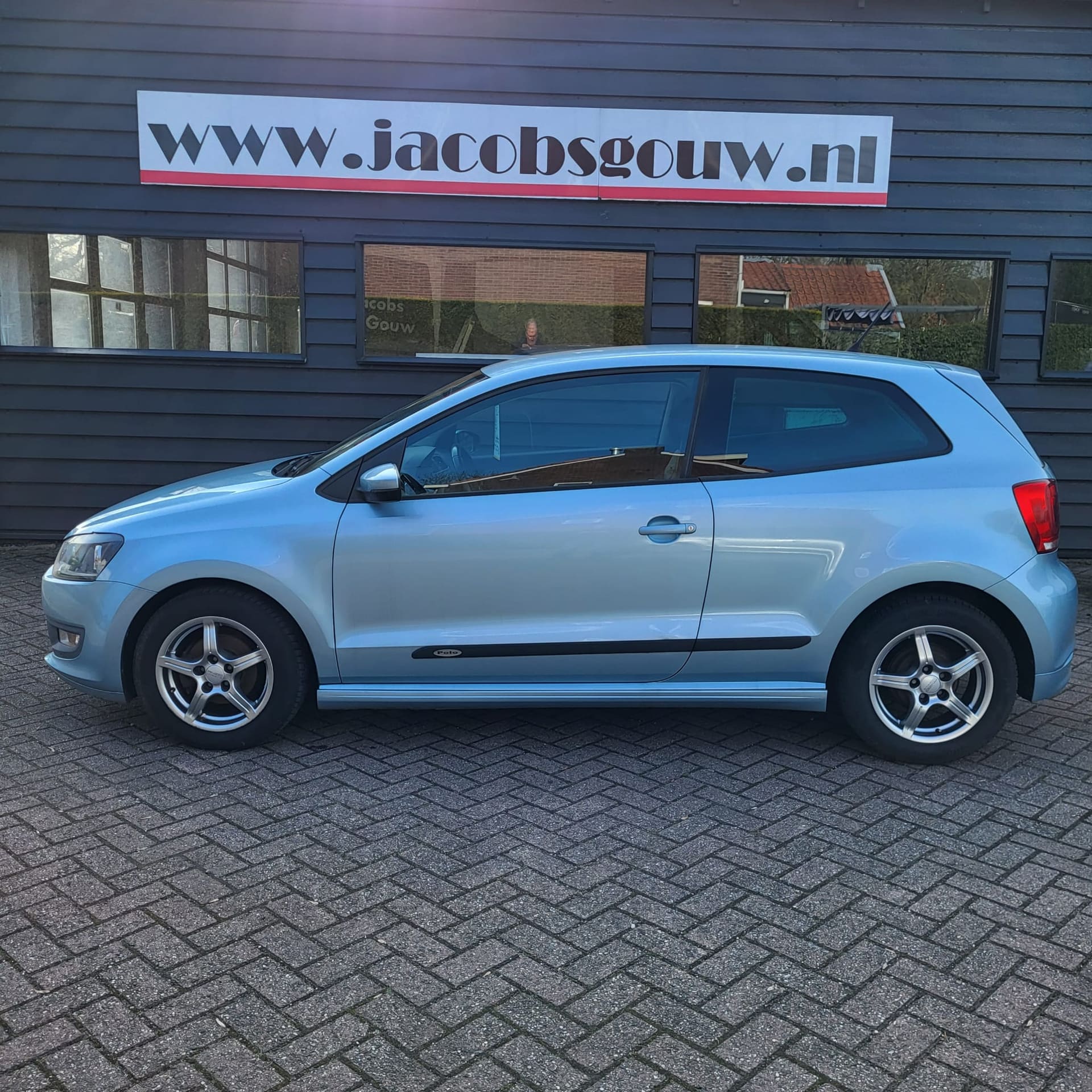 Lichtblauwe Volkswagen Polo voor de donkere gevel van het bedrijf